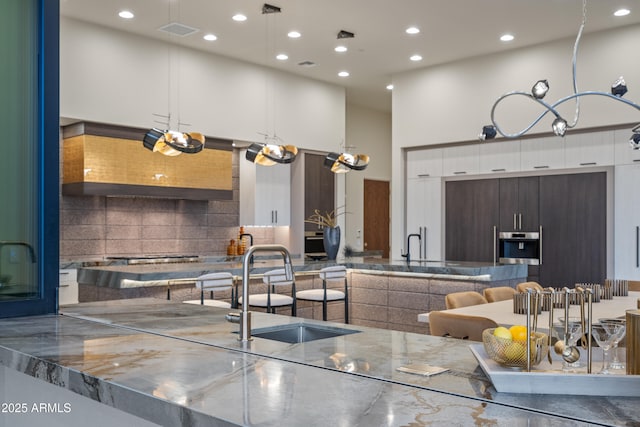 kitchen featuring stainless steel appliances, visible vents, a towering ceiling, a sink, and modern cabinets