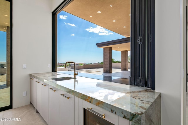 kitchen with modern cabinets, white cabinetry, light stone counters, and a sink