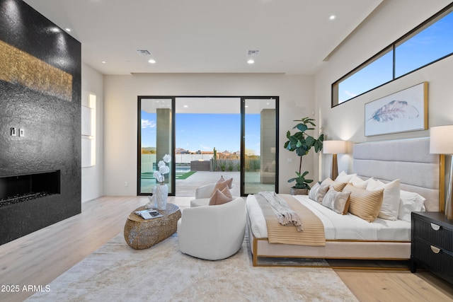 bedroom featuring recessed lighting, a large fireplace, wood finished floors, visible vents, and access to outside