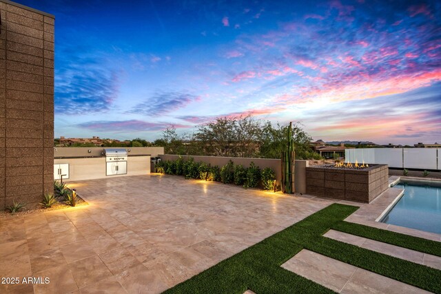 patio terrace at dusk with exterior kitchen, fence, and a fenced in pool