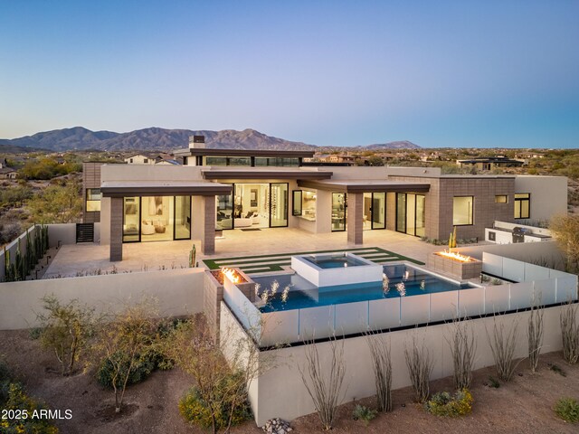 rear view of property featuring a patio, a pool with connected hot tub, a fenced backyard, and a mountain view