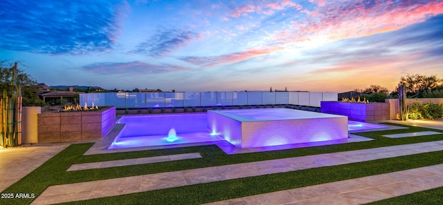 pool at dusk with fence private yard, an outdoor pool, a yard, and a jacuzzi