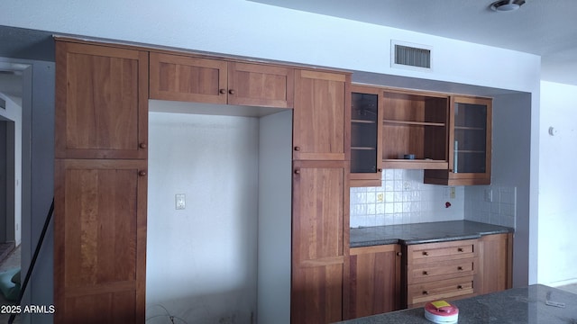 kitchen featuring tasteful backsplash, dark countertops, brown cabinets, and visible vents