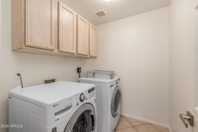 clothes washing area with cabinets, washer and dryer, and light tile patterned floors