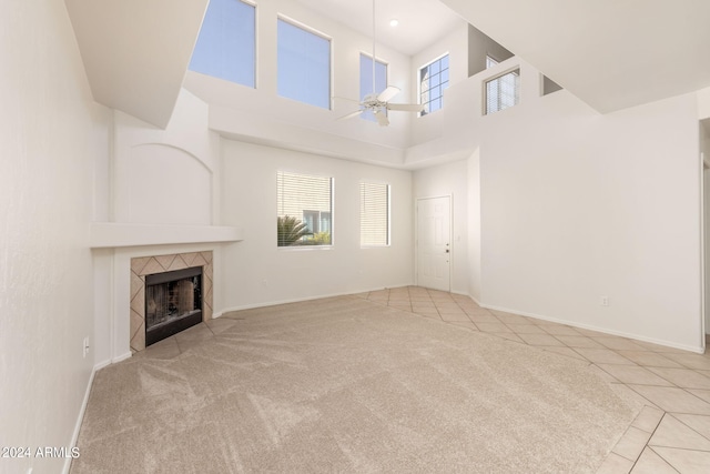 unfurnished living room featuring a high ceiling, a tiled fireplace, ceiling fan, and light tile patterned flooring