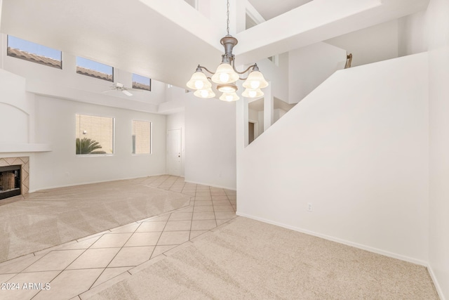 unfurnished living room with ceiling fan with notable chandelier, a towering ceiling, light tile patterned floors, and a fireplace