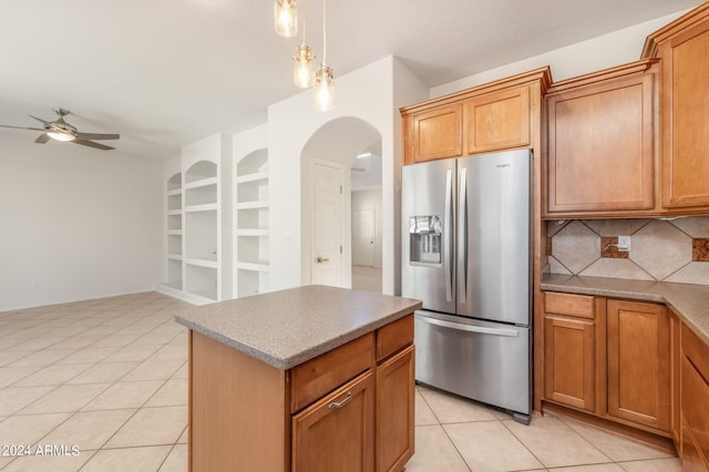 kitchen with ceiling fan, stainless steel fridge, light tile patterned floors, a kitchen island, and backsplash