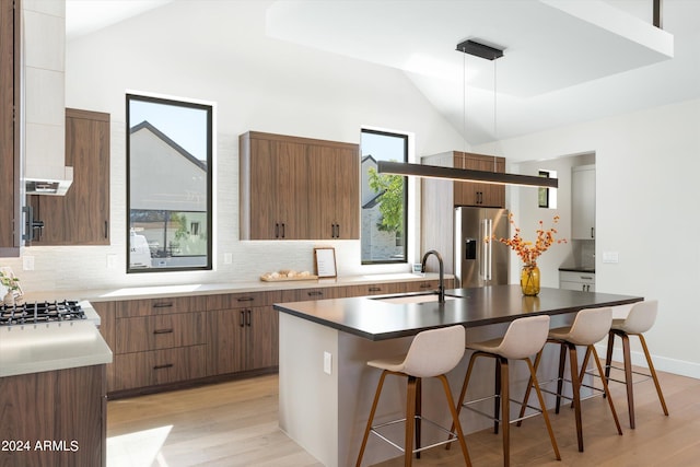 kitchen with sink, decorative light fixtures, lofted ceiling, high quality fridge, and a center island with sink