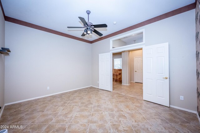 tiled empty room featuring ceiling fan and crown molding