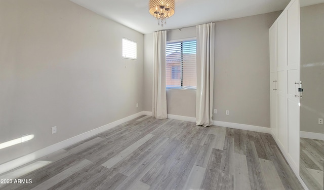 spare room featuring an inviting chandelier and light hardwood / wood-style floors