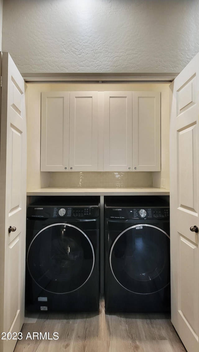 laundry room featuring cabinets, independent washer and dryer, a textured ceiling, and light wood-type flooring