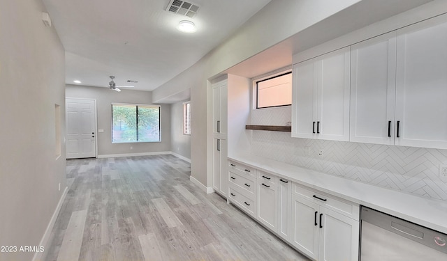 kitchen with light wood-type flooring, stainless steel dishwasher, white cabinets, ceiling fan, and backsplash