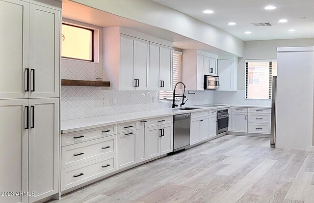 kitchen featuring white cabinetry, stainless steel appliances, backsplash, and light hardwood / wood-style flooring