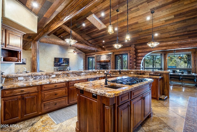 kitchen featuring an island with sink, rustic walls, hanging light fixtures, wood ceiling, and gas stovetop