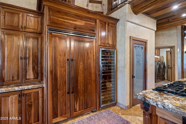 kitchen with stone counters, wine cooler, stainless steel gas cooktop, paneled built in fridge, and washing machine and dryer