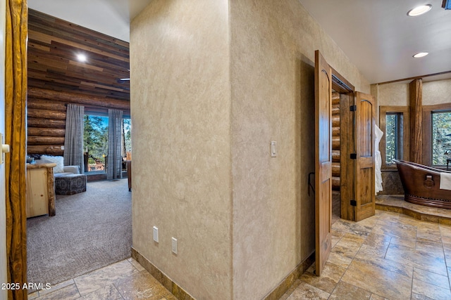 hallway featuring log walls, plenty of natural light, and light colored carpet