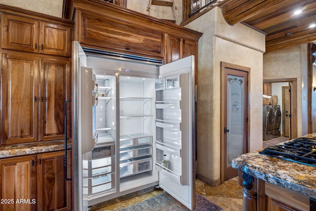 kitchen featuring refrigerator, dark stone counters, separate washer and dryer, and black gas stovetop