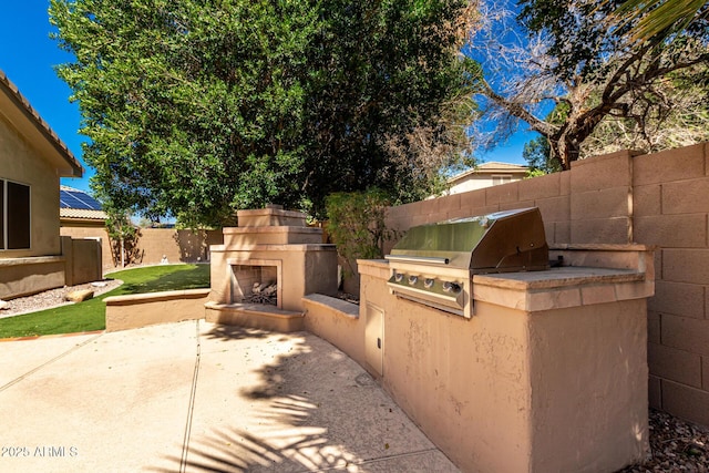 view of patio / terrace featuring exterior kitchen, a fenced backyard, exterior fireplace, and a grill