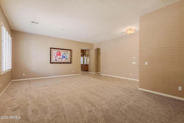 spare room with visible vents, light colored carpet, arched walkways, and baseboards