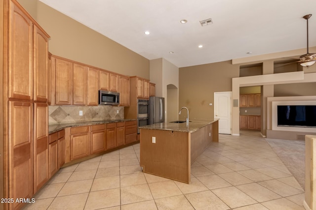 kitchen featuring dark stone countertops, a center island with sink, arched walkways, a sink, and appliances with stainless steel finishes