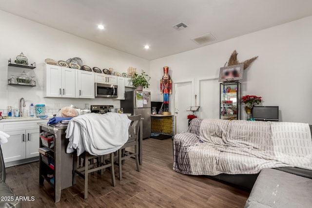 kitchen with dark wood-type flooring, white cabinets, sink, appliances with stainless steel finishes, and a kitchen bar