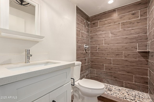 bathroom with a tile shower, vanity, and toilet