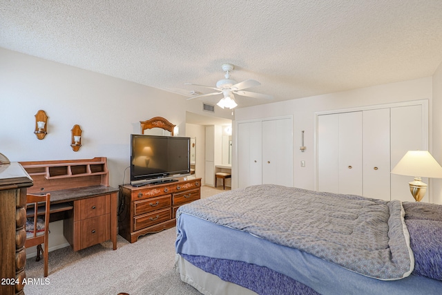 bedroom with multiple closets, ceiling fan, light carpet, and a textured ceiling