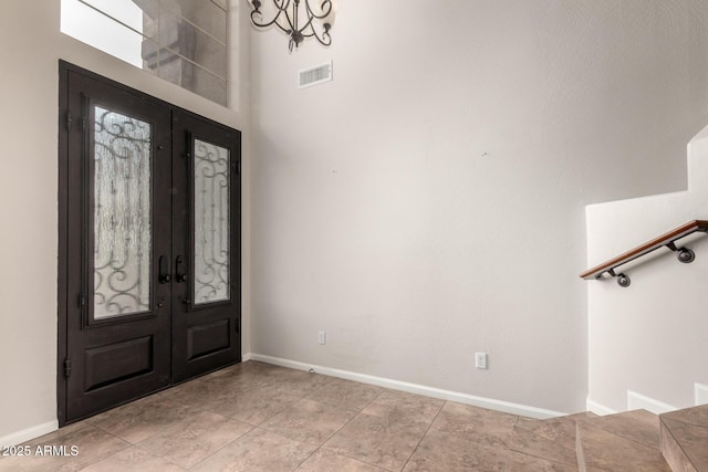 entryway with a notable chandelier, light tile patterned floors, french doors, and a towering ceiling