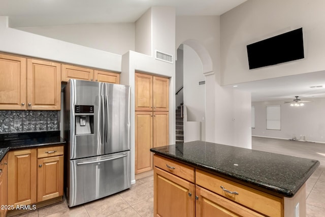 kitchen with high vaulted ceiling, decorative backsplash, dark stone counters, light tile patterned floors, and stainless steel refrigerator with ice dispenser