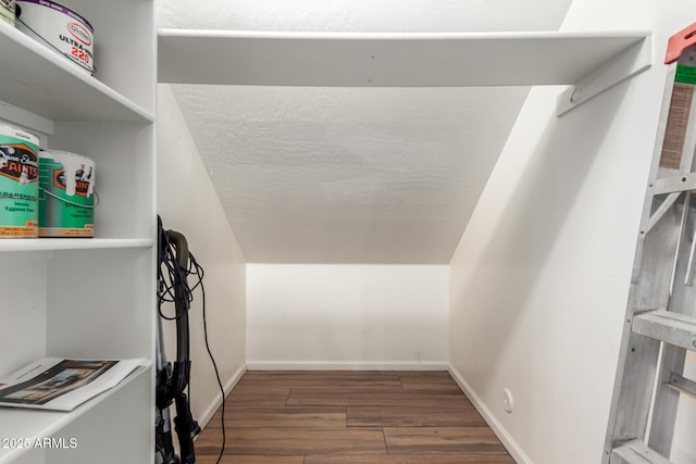 walk in closet with dark wood-type flooring and vaulted ceiling