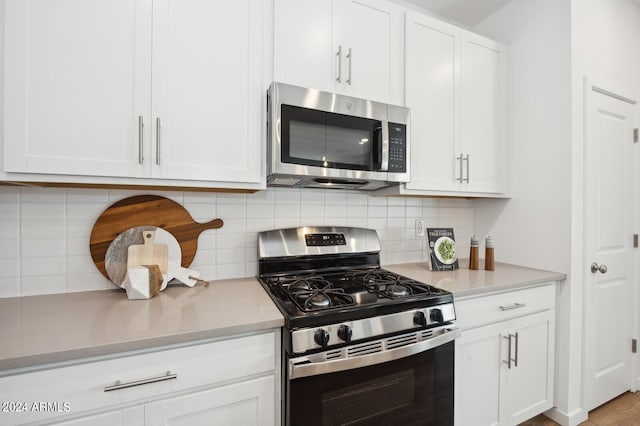 kitchen with decorative backsplash, white cabinets, stainless steel appliances, and light hardwood / wood-style floors