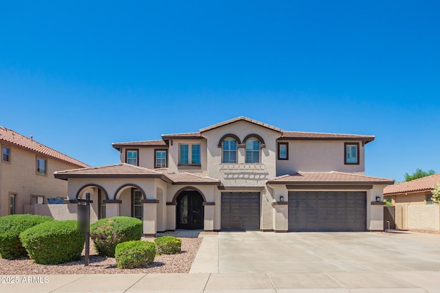 mediterranean / spanish-style home with a tile roof, concrete driveway, an attached garage, fence, and stucco siding
