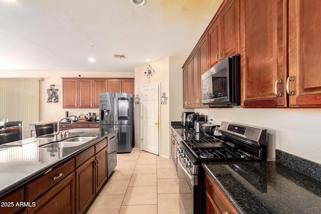 kitchen with dark stone countertops, a sink, light tile patterned floors, stainless steel appliances, and visible vents