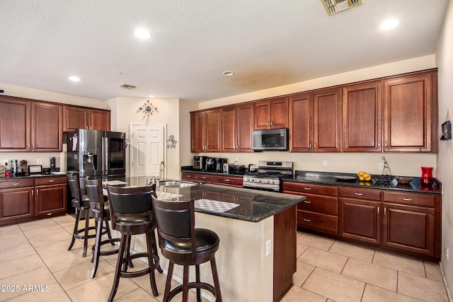kitchen featuring a sink, light tile patterned floors, stainless steel appliances, a kitchen bar, and visible vents