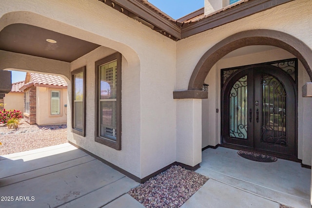 entrance to property with a tiled roof, french doors, and stucco siding