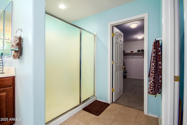 full bathroom with tile patterned floors, vanity, a shower stall, and a walk in closet