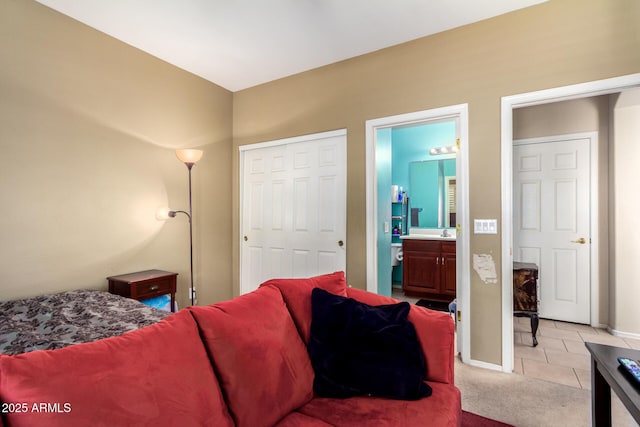 bedroom featuring a closet, connected bathroom, light tile patterned floors, light colored carpet, and baseboards