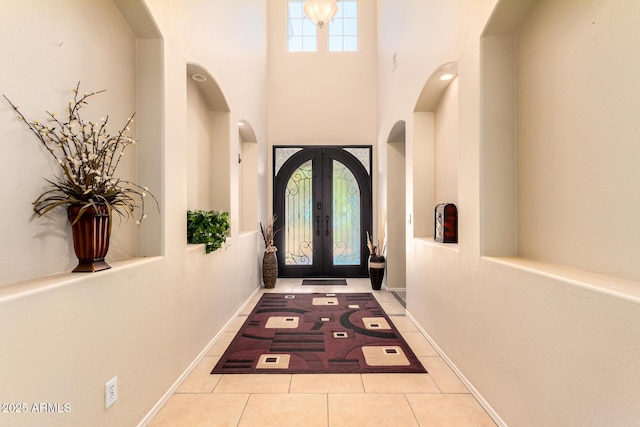 doorway with tile patterned floors, arched walkways, french doors, a towering ceiling, and baseboards