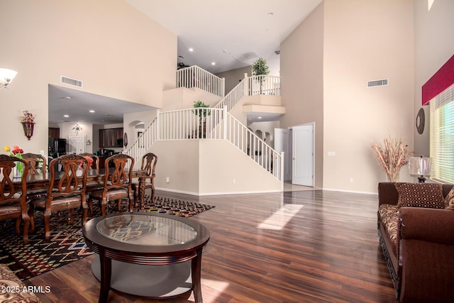 living room featuring wood finished floors, visible vents, a towering ceiling, and stairs