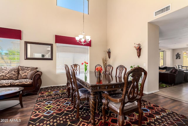 dining room featuring wood finished floors, baseboards, a high ceiling, a notable chandelier, and visible vents