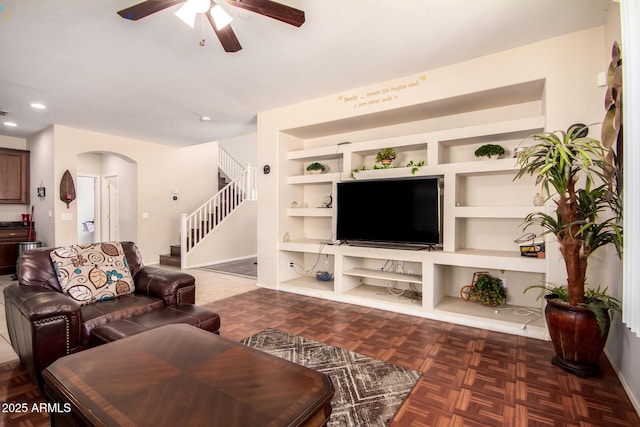 living room featuring stairway, arched walkways, a ceiling fan, and built in features