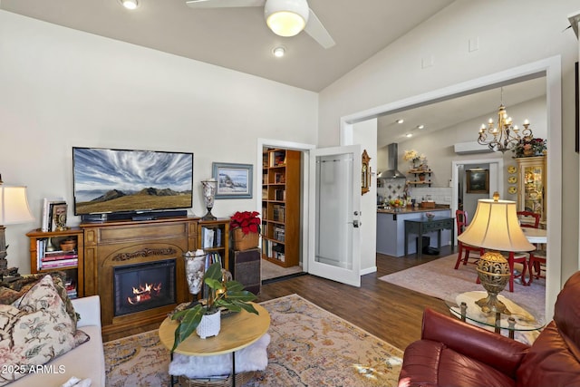 living room featuring a glass covered fireplace, lofted ceiling, wood finished floors, ceiling fan with notable chandelier, and recessed lighting