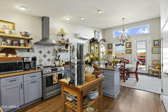 kitchen featuring dark wood-style floors, appliances with stainless steel finishes, gray cabinetry, wall chimney range hood, and open shelves