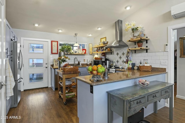 kitchen with a peninsula, wall chimney range hood, a wall mounted AC, appliances with stainless steel finishes, and open shelves