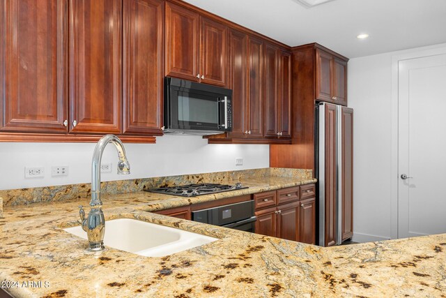 kitchen with stainless steel gas cooktop, sink, light stone counters, high end refrigerator, and oven