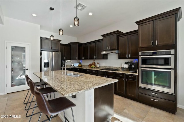kitchen featuring visible vents, a sink, appliances with stainless steel finishes, under cabinet range hood, and light stone counters