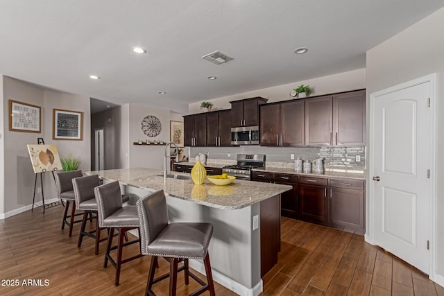 4108 N 304th Ln, Buckeye, AZ 85396 - kitchen with stainless steel appliances, dark wood-style flooring, decorative backsplash, a kitchen bar, and light stone counters