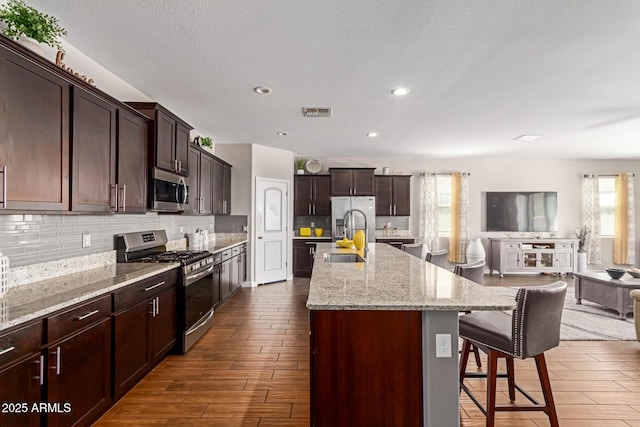 4108 N 304th Ln, Buckeye, AZ 85396 - kitchen featuring appliances with stainless steel finishes, a kitchen bar, dark wood finished floors, decorative backsplash, and an island with sink