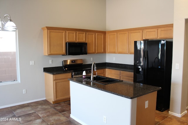 kitchen featuring a towering ceiling, sink, black appliances, dark stone countertops, and an island with sink