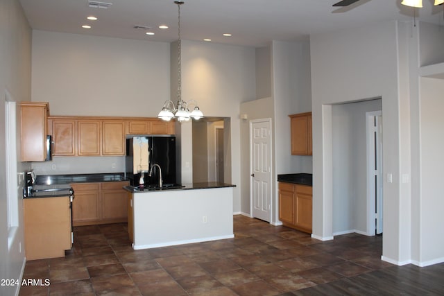 kitchen featuring a kitchen island with sink, a high ceiling, black refrigerator, hanging light fixtures, and sink